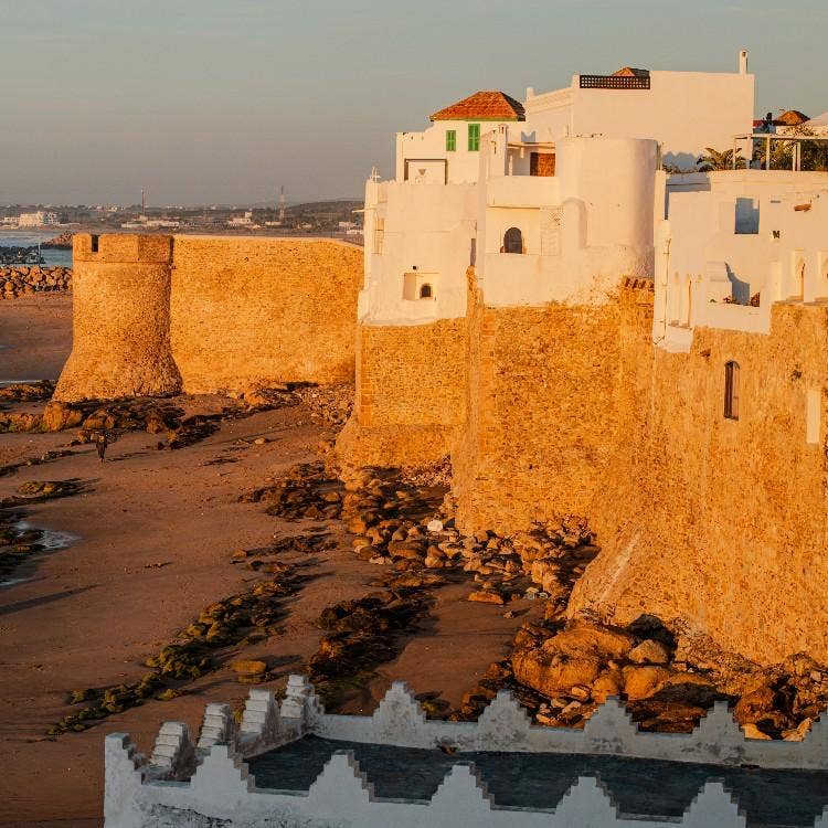 White buildings built on the ancient stone ramparts of the medina along the Atlantic coast in Asilah, Morocco at sunset.