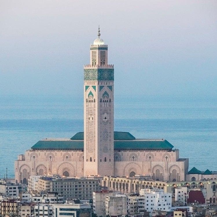 The grand Hassan II Mosque featuring a tall minaret overlooking the blue Atlantic Ocean and city buildings in Casablanca, Morocco.