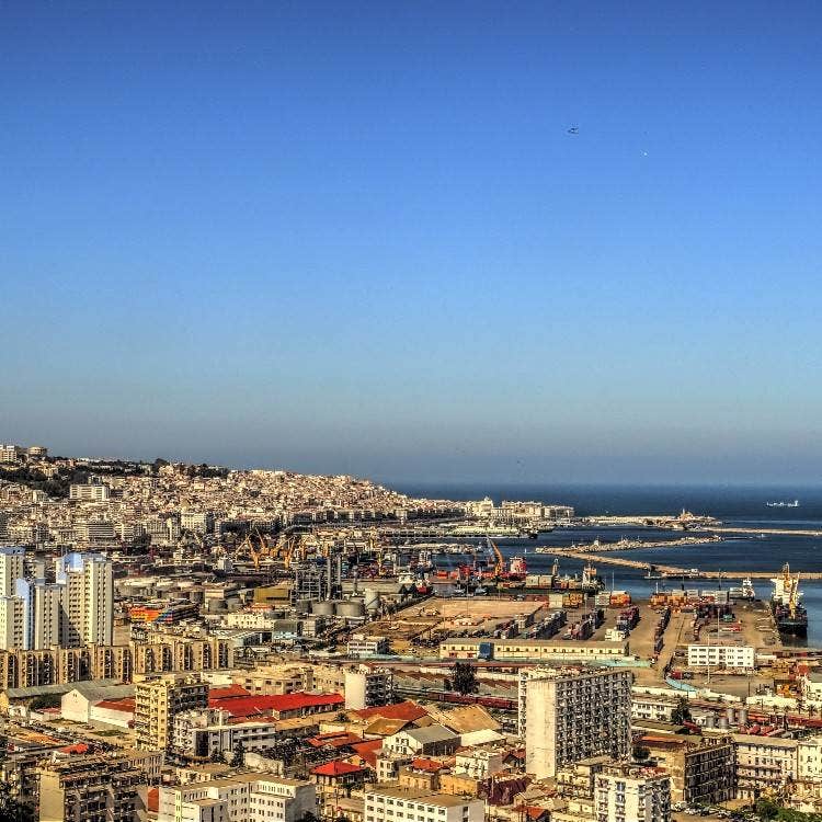 A wide aerial view of the bustling city harbor and port facilities along the Mediterranean Sea coastline in Algiers, Algeria.