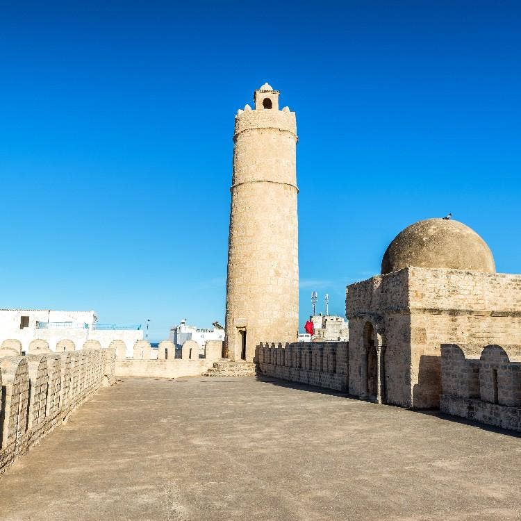 The stone watchtower and domed structure of the ancient Ribat fortress under a clear blue sky in Sousse, Tunisia.
