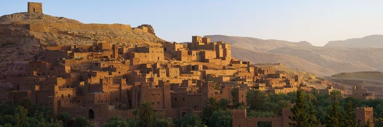 A panoramic view of the ancient, earthen clay fortified village of Aït Benhaddou in Morocco under a blue sky.