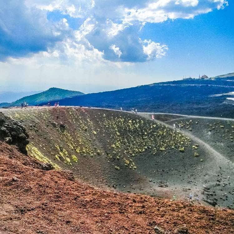 A wide panoramic shot of the volcanic Silvestri Craters on Mount Etna, featuring dramatic ash slopes, pathways, and distant hills.