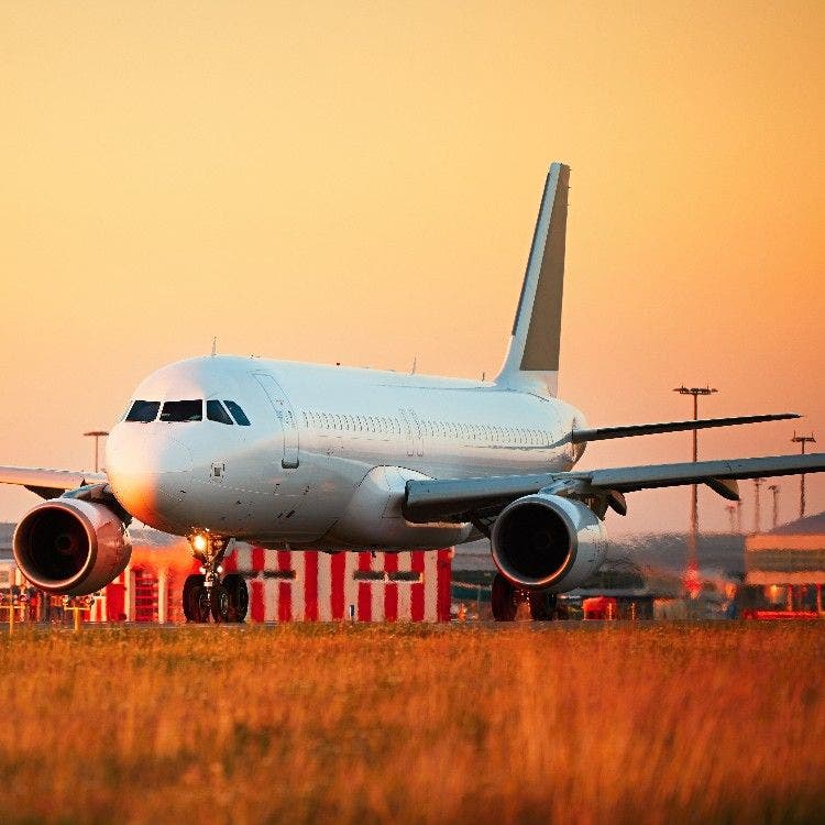 A passenger airplane preparing for takeoff on an airport runway, bathed in warm golden hour light during sunset.
